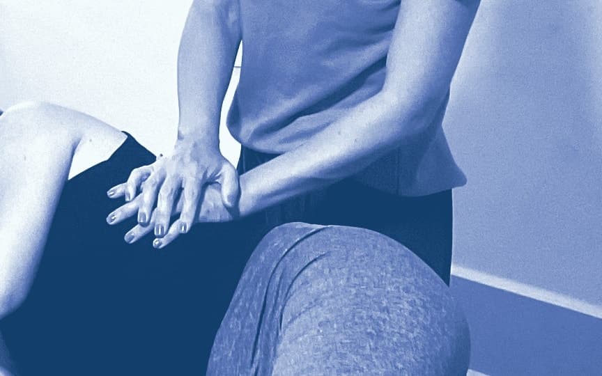 A therapist with hands stacked on a patient’s hip, on the table