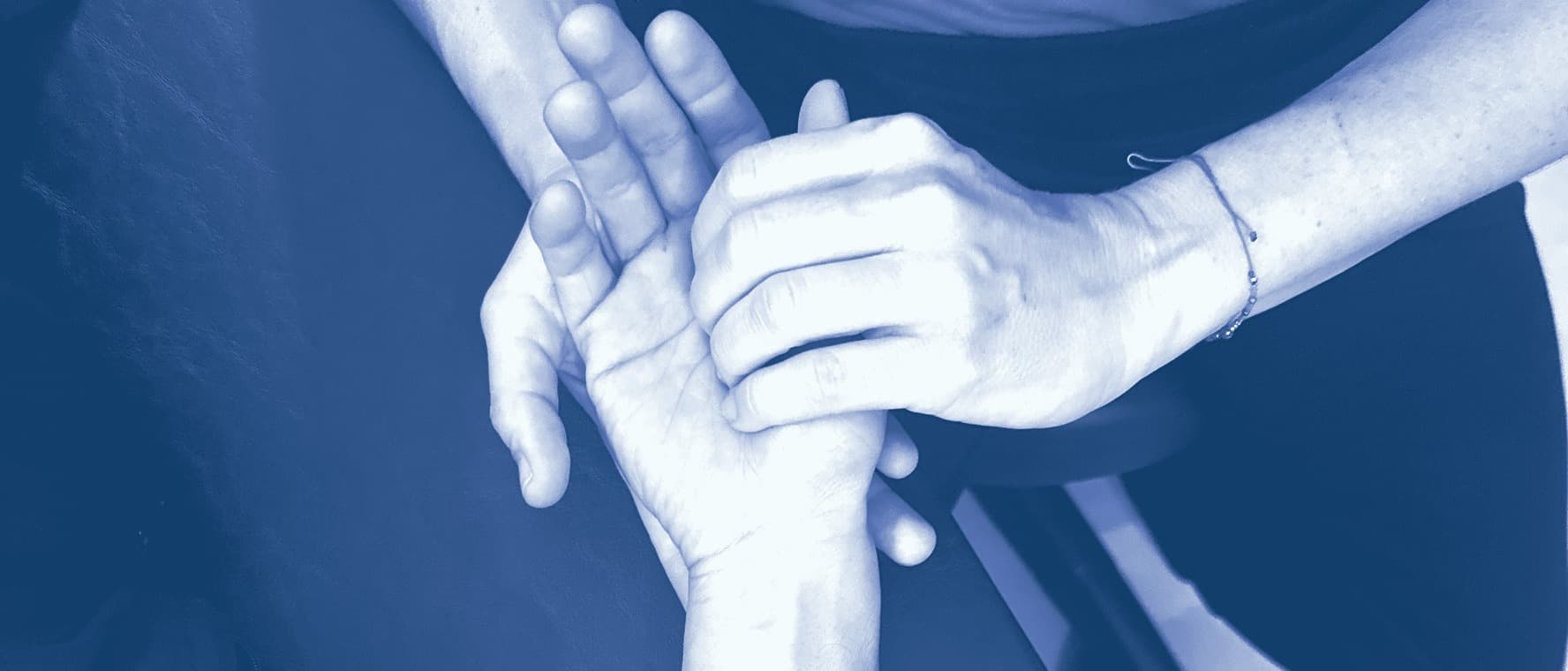 A therapist’s hands holding a patient’s hand with a light touch